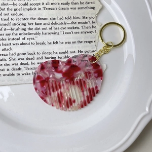 Detail of heart-shaped acetate mini comb keychain with red marble texture on ceramic tray