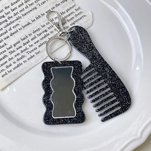 Detail of a vintage black glitter comb and mirror keychain on an elegant ceramic plate