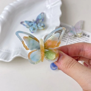 Détail macro d'une pince à cheveux papillon en acétate coloré tenue à la main sur plateau