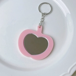 Detalle del llavero de acrílico rosa con forma de manzana, espejo de corazón y cadena plata