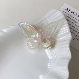 Détail macro d'une pince à cheveux papillon aux reflets irisés sur une assiette blanche