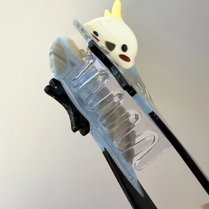 Macro detail of bird hair claw clip showing translucent blue teeth and cockatiel design