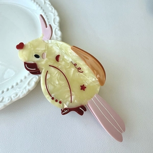 Detail of a parrot hair claw made of marble yellow acetate with pink crest and heart patterns