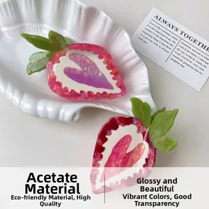 Close-up of strawberry acetate hair claw clips with translucent red gradient and green leaves