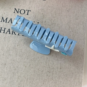 Close-up of a blue glossy hair claw clip with white star details on textured fabric