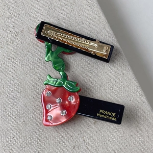 Close-up of strawberry hair clip with rhinestones and golden metal duckbill clamp