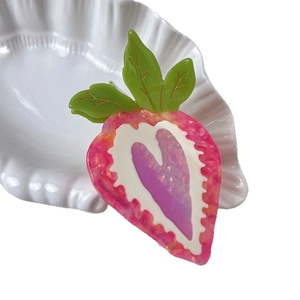 Cute strawberry acetate hair claw with green leaf and purple heart center on white tray