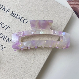 Close-up of rectangular purple marble acetate hair claw clip on a beige book