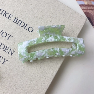 Large green marble acetate hair claw clip for women on a vintage style book background