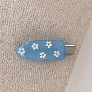 Dettaglio di fermaglio per capelli azzurro con piccoli fiori 3D bianchi e centri dorati