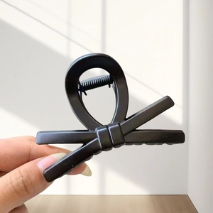 Detail of matte black bow hair claw clip showing a thick resin design in a hand