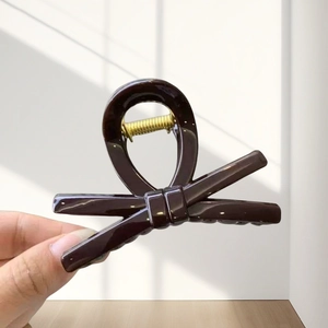 Close-up of a large dark brown bow hair claw clip with a glossy finish and gold metal spring