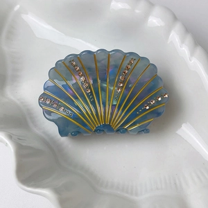 Detail of shell-shaped blue acetate hair claw with rhinestones on a white plate