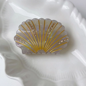 Close-up of shell-shaped acetate hair claw with iridescent finish and rhinestone accents