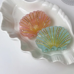 Detail of shell-shaped hair claws with golden radiating textures and rhinestones