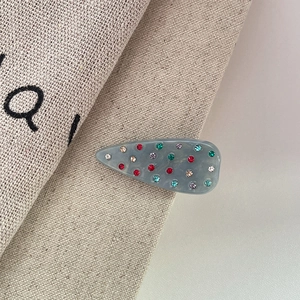 Dettaglio del fermaglio per capelli a goccia in resina con strass colorati su tela beige