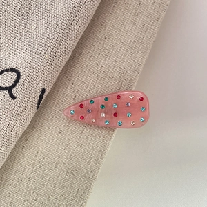 Dettaglio di fermaglio per capelli rosa con strass multicolori su tessuto a trama