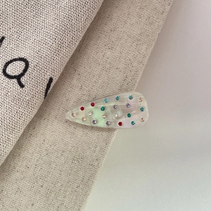 Dettaglio del fermaglio per capelli a goccia iridescente con strass colorati su lino