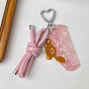 Détail d'un peigne en acétate rose marbré avec ours brun et porte-clés en forme de cœur