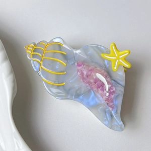 Macro detail of ocean conch hair claw clip in marble blue acetate with yellow starfish