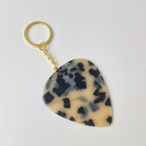 Detail shot of a guitar pick keychain with marble texture and golden metal ring