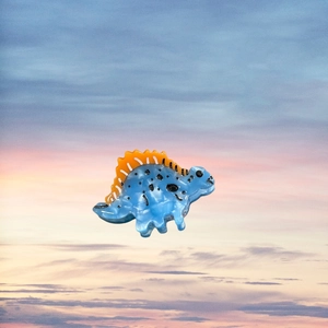 Pince à cheveux dinosaure bleue avec pointes orange sur fond de coucher de soleil