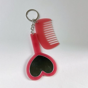 Détail du porte-clés avec miroir en cœur rose translucide et mini peigne pour sacs