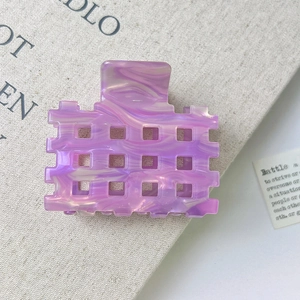 Detail shot of purple marble acetate hair claw clip with cutout grid design on beige book
