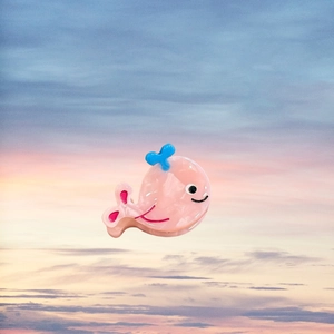 Vue détaillée de la pince à cheveux baleine rose avec jet d'eau bleu sur fond de coucher