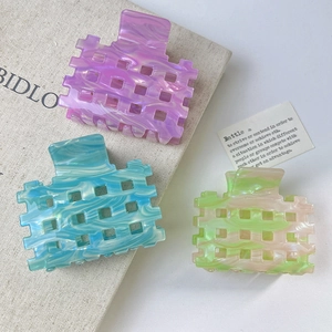 Hollow grid acetate hair claws in purple marble and blue teal colors on linen books