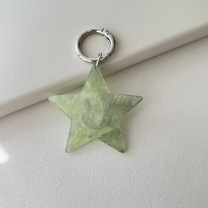 Macro detail of green glitter acrylic star keychain with a smiling face and metal ring