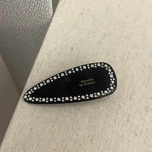 Detail of a black French barrette with colorful rhinestones and gold lettering on fabric