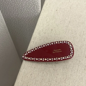 Macro view of red teardrop hair clip with rhinestones and gold Barrette lettering