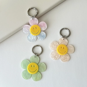 Three colorful acrylic smiling flower keychains with silver hooks on a neutral surface