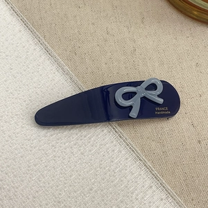 Detailed shot of handmade acetate hair clip with blue bow and gold engraved logo text