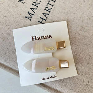 Close-up of pearl white hair clips with gold lettering on a rustic linen background