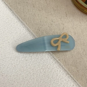 Detail of blue acetate hair clip with cream bow and handmade text on linen fabric
