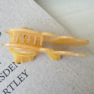 Close-up of amber acetate hair claw clip with a cute fish design on beige fabric