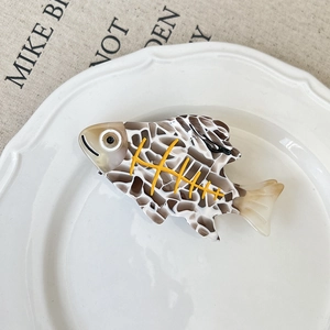 Détail d'une pince à cheveux en forme de poisson avec motif écaille brune sur assiette