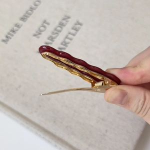 Macro view of the open golden metal base and burgundy wave textured duckbill hair clip