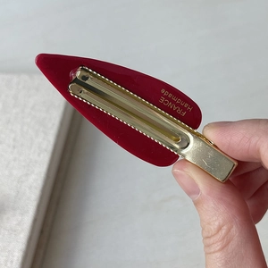 Dettaglio ravvicinato di fermaglio in acetato rosso scuro con base dorata e incisione a mano