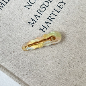 Close-up of wavy acetate hair clip with pink marble pattern and gold metal clasp