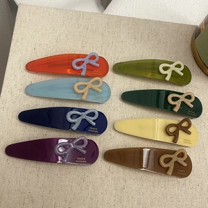 Set of 8 colorful acetate hair clips with 3D bows and teardrop shapes on white fabric