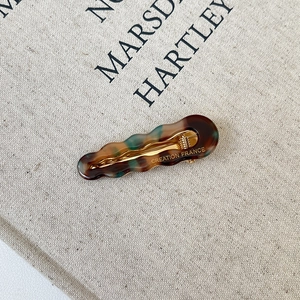 Close-up of wave-shaped tortoiseshell acetate hair clip with gold metal duckbill clip