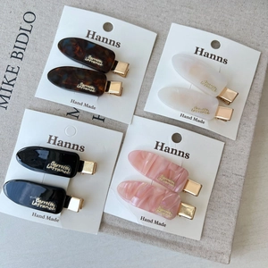 Set of four colorful acetate hair clips with gold logo on a minimalist background