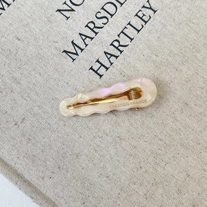 Detail shot of wavy acetate hair clip with pearlescent finish and gold metal duckbill clamp