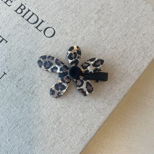 Detailed top view of a leopard print five-petal flower hair clip on a soft gray textile