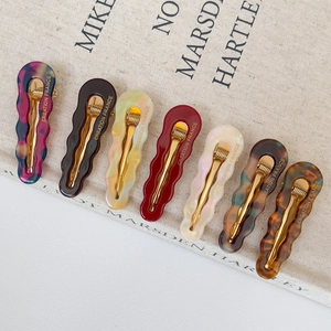 Set of 7 colorful wave-shaped acetate hair clips with gold metal base on elegant fabric