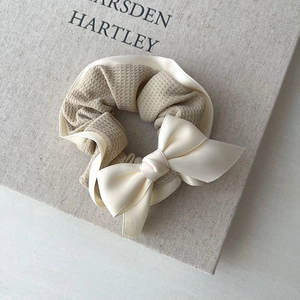 Detail of cream scrunchie featuring waffle texture fabric and a large satin bow accent