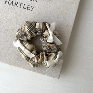 Close-up of yellow checkered scrunchie with white bows on minimalist book background
